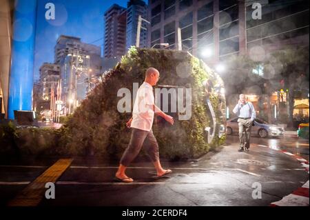 I pedoni si fanno strada lungo Sukhumvit Rd. Bangkok, Thailandia durante una forte caduta di pioggia. La pioggia cade anche sull'obiettivo. Foto Stock