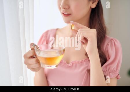 Giovane donna con un bicchiere d'acqua che prende la pillola di vitamina a casa Foto Stock