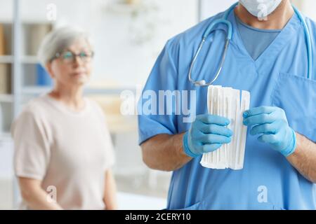 Medico irriconoscibile in uniforme blu e guanti che estrano il test bastone per la paziente anziana seduta dietro di lui Foto Stock