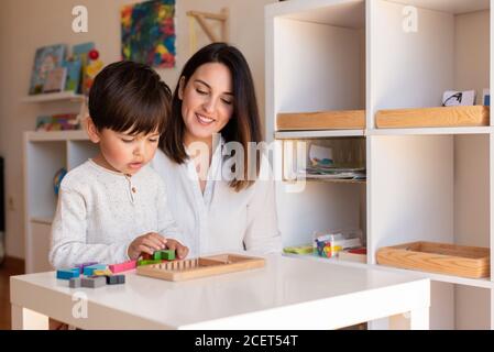 Lillte Kid giocare con un puzzle di legno di tetris e la madre o l'aiuto dell'insegnante. Homeshooling. Comunità di apprendimento. Scuola Montessori Foto Stock