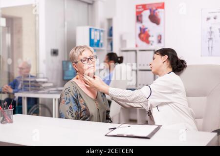 Il medico tocca il collo del paziente anziano per le anomalie delle ghiandole negli uffici ospedalieri. Medico che esamina la donna anziana. Foto Stock