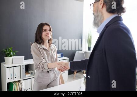 Giovane donna sicura che saluta il manager delle risorse umane maturo con la stretta di mano prima iniziare il colloquio di lavoro Foto Stock