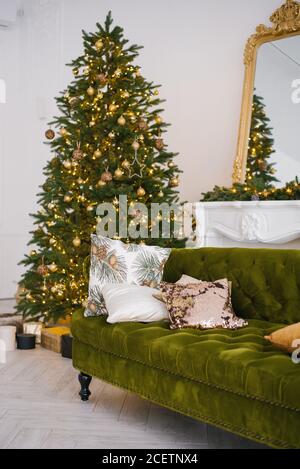 Il divano verde in velluto con cuscini nella luminosa mansarda la camera dispone di un camino artificiale. UN ampio soggiorno con bianco Mura e un Cristo decorato Foto Stock