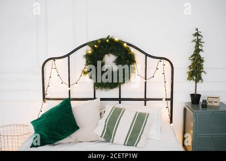 Natale e composizione del nuovo anno. Camera scandinava con biancheria da letto bianca e verde con decorazioni natalizie fatte di rami di abete, ghirlande e. Foto Stock