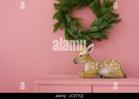 Souvenir fawn su un dresser rosa contro una parete rosa su cui pende un albero di Natale. Spazio di copia Foto Stock