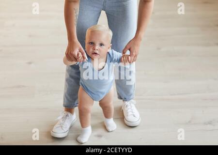 Vista ad alto angolo di una donna irriconoscibile che indossa jeans aiutando il suo bambino a camminare, copia spazio Foto Stock