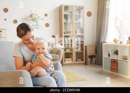 Ritratto orizzontale di felice giovane donna seduta su poltrona con il suo bambino sul giro sorridente, copia spazio Foto Stock