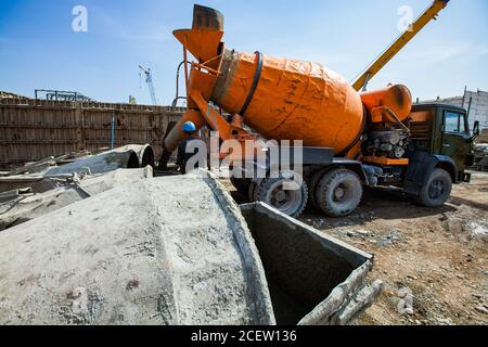 Vecchio impianto di fertilizzante fosfato in modernizzazione. Costruzione di nuovi edifici industriali. Gru mobile, operatori, autocarro con betoniera arancione e benna per cemento Foto Stock