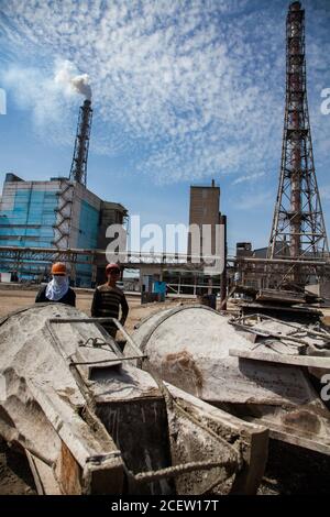 Vecchio impianto di fertilizzante fosfato in modernizzazione. Costruzione di nuovi edifici industriali. Lavoratori con secchi di cemento. Fumo camino e industriale Foto Stock