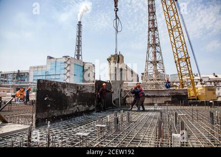 Vecchio impianto di fertilizzante fosfato in modernizzazione. Lavoratori con secchio di cemento riempimento di rinforzo del nuovo seminterrato dell'edificio. Su edifici industriali, Foto Stock