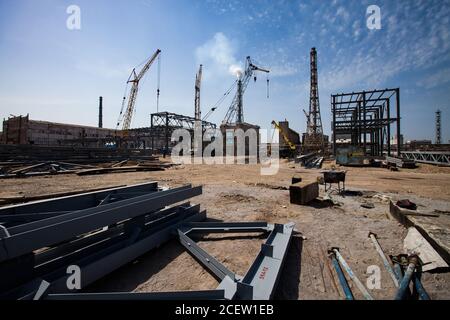 Gru mobili e camino di fabbrica su cielo blu con nuvole. Griglie metalliche grigie posate a terra. Vista panoramica assemblaggio di edifici industriali. Foto Stock