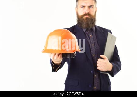 Ispezione, attrezzatura, concetto di protezione. Casco da costruzione nelle mani dell'ispettore dell'edificio. L'uomo con la bearded tiene isolato il casco su bianco. Supervisore delle costruzioni con documenti e faccia seria. Foto Stock
