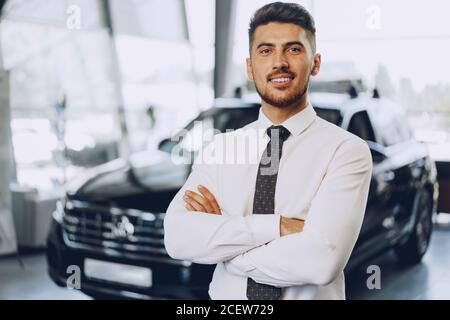 Amichevole bel venditore di auto uomo in piedi in salone di auto Foto Stock