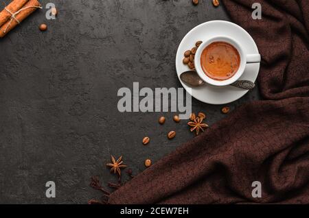 Composizione autunnale. Tazza di caffè, sciarpa di pashmina marrone, chicchi di caffè, bastoncini di cannella su sfondo nero. Umore autunnale. Disposizione piatta. Spazio di copia Foto Stock