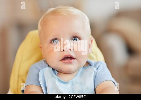 Primo piano ritratto di carino bambino seduto su sedia alta in attesa di cibo guardando la fotocamera, copia spazio Foto Stock