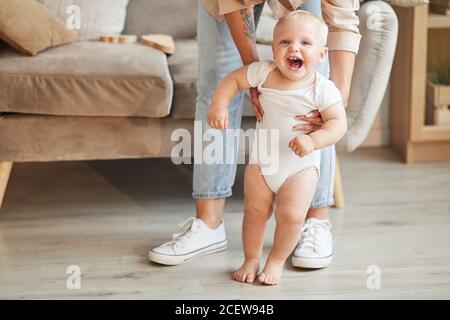 Sezione bassa scattata di donna irriconoscibile che indossa jeans che aiuta il suo bambino allegro con imparare a camminare, spazio di copia Foto Stock