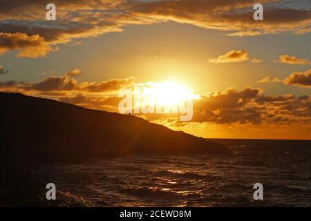 Splendido scenario del mare illuminato dal sole con un tramonto dorato sul promontorio di Trefor, Galles del Nord Foto Stock