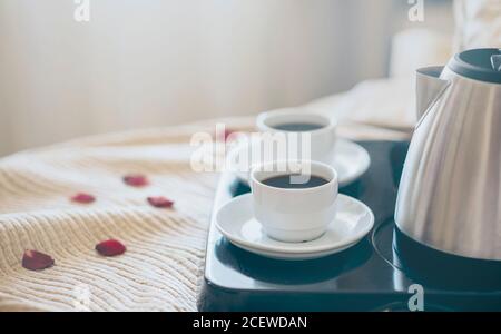 La colazione del mattino con caffè nero in camera da letto. Due tazze di caffè sul letto decorato con petali di rosa in hotel di lusso in camera da letto. Foto Stock