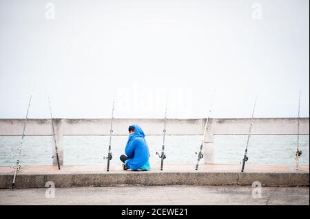 Un pescatore solista si siede in attesa di un boccone in un molo a Bang Saen, vicino Pattaya Thailandia. Foto Stock