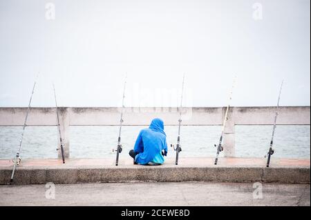 Un pescatore solista si siede in attesa di un boccone in un molo a Bang Saen, vicino Pattaya Thailandia. Foto Stock