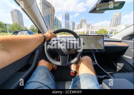 Persona che guida una nuova vettura Tesla. L'interno di una Tesla Model 3 AWD a lungo raggio, completamente elettrica, con una portata di 320 miglia Foto Stock