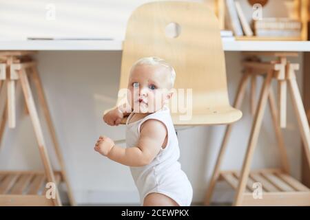 Bambino caucasico che tiene sulla sedia imparando a stare in piedi sulle gambe copia spazio Foto Stock