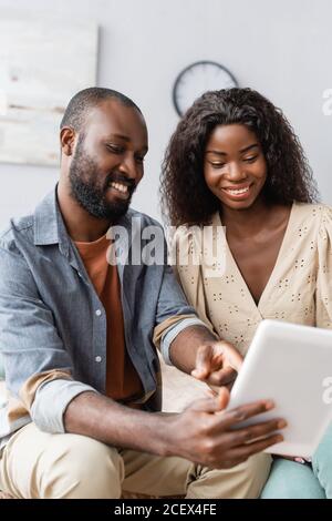 fuoco selettivo dell'uomo afroamericano che punta con il dito tablet digitale vicino a moglie Foto Stock