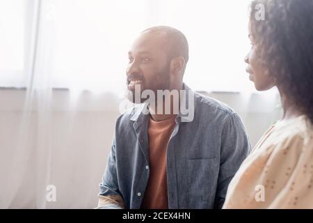 fuoco selettivo della moglie afroamericana che guarda il marito eccitato a casa Foto Stock
