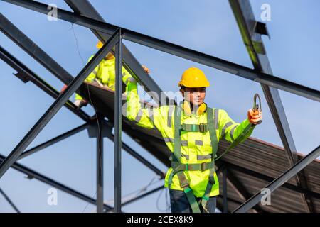 I lavoratori asiatici della costruzione del tetto indossano l'attrezzatura di altezza di sicurezza per installare il telaio del tetto, dispositivo anticaduta per il lavoratore con ganci per il corpo di sicurezza harn Foto Stock