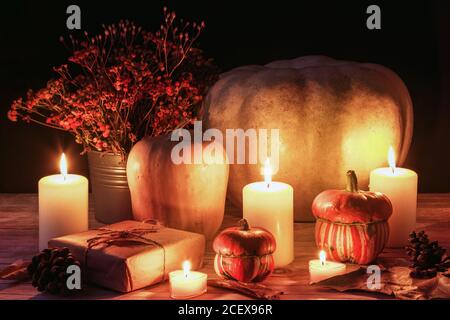 Layout autunnale con zucche, candele brucianti e fiori d'arancio in cesto. Concetto di ringraziamento. Sfondo nero, messa a fuoco selettiva. Foto Stock