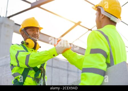 I lavoratori asiatici indossano attrezzature di sicurezza altezza costruzione, lavoro di squadra, partnership, gesto e concetto di persone - primo piano di costruttori mani in guanti di saluto Foto Stock