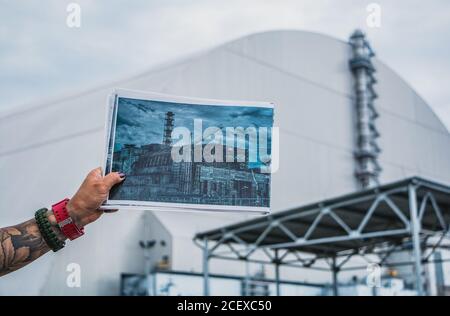 Una foto di qualcuno che mostra una foto del vecchio sarcofago che ha protetto il quarto reattore della centrale nucleare di Cernobyl in parte anteriore del n Foto Stock