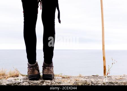 Un'escursionista femminile non riconoscibile con bastone da trekking in piedi sulla pietra confina con il cielo nuvoloso grigio e godendo la libertà durante il pellegrinaggio Attraverso la Spagna Foto Stock