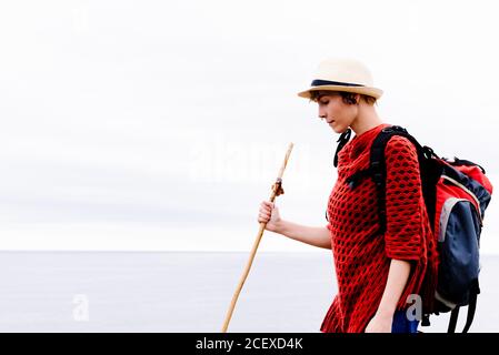 Vista laterale della donna escursionista con zaino e bastone da trekking in piedi contro il cielo nuvoloso grigio e godendo la libertà durante il pellegrinaggio Attraverso la Spagna Foto Stock