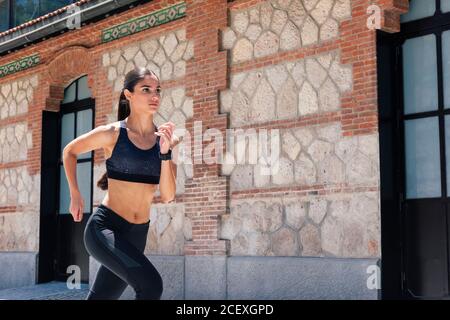 Indossa gli abiti sportivi che corrono velocemente lungo il marciapiede durante l'allenamento il giorno di sole in città Foto Stock