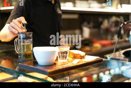 barista maschile irriconoscibile in piedi al bancone e versare una bevanda calda in tazza mentre si lavora in un'accogliente caffetteria Foto Stock