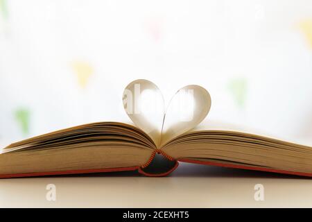 Primo piano del libro aperto con pagine a forma di cuore posto sul tavolo in una stanza luminosa Foto Stock