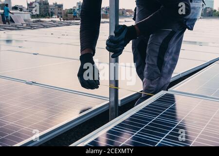 Operatore in uniforme protettiva che installa pannelli solari moderni sul tetto di edificio industriale Foto Stock