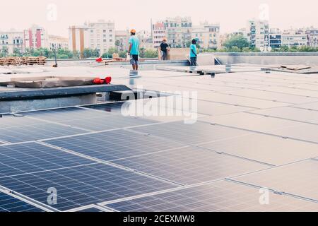 Azienda di lavoratori etnici maschi che installano pannelli solari contemporanei in cantiere di fabbrica Foto Stock