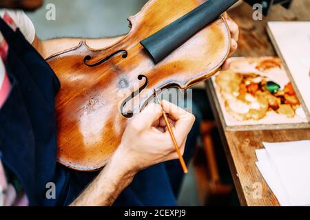 Vista laterale di raccolto anonimo artigiano pittura antico violino durante lavori di restauro in officina Foto Stock