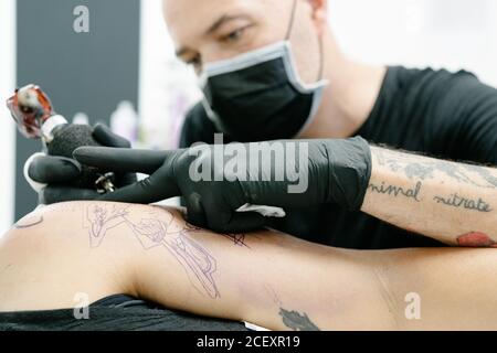 Tatuaggio maschile raccolto con macchina che fa tatuaggio sul braccio di Donna sdraiata sul tavolo in salone Foto Stock