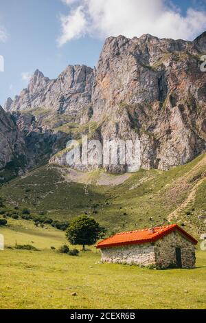 Maestoso paesaggio della catena montuosa Picos de Europa e piccolo cabina di pietra situata sul prato verde il giorno di sole in Asturie Foto Stock