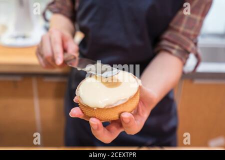 Persona non riconoscibile tagliata in piedi al tavolo e riempire le crostate shortcrust con crema in cucina Foto Stock