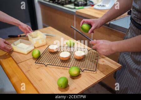 Crop uomo e donna in grembiuli che fanno crostate con cagliata e scorza di calce lavorando insieme al tavolo da cucina Foto Stock