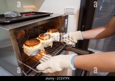 cuocete senza volto in guanti prendendo rack con forme di soufflé fuori dal forno caldo a casa Foto Stock