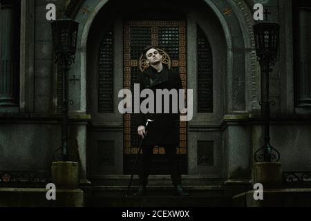 Giovane ed elegante vampiro di fronte ad un mausoleo in un cimitero Foto Stock