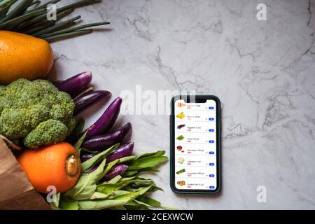 Vista dall'alto di frutta e verdura assortite in sacchetto di carta organizzato sul tavolo con smartphone con app per lo shopping online e consegna Foto Stock