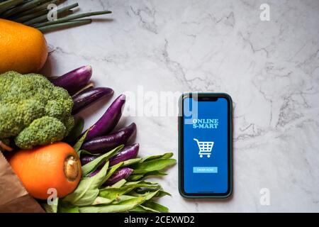 Dall'alto dei generi alimentari consegnati in un sacchetto di carta posizionato sopra tavolo con cellulare con app mobile per lo shopping online Foto Stock