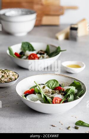 Dall'alto di ciotole con deliziosa insalata a base di pesce e spinaci verdi con pomodori ciliegini tritati e olive nere guarnito con semi Foto Stock