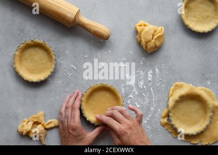 Vista dall'alto della casalinga anonima di raccolto che riempie le forme metalliche con pasta sfoglia mentre prepari la torta al limone in cucina Foto Stock